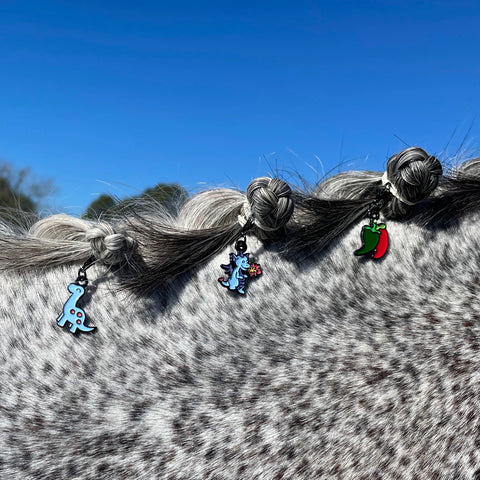 pinsnickety brontosaurus, dragon, and chili peppers bridle charms in a grey horse's braided mane