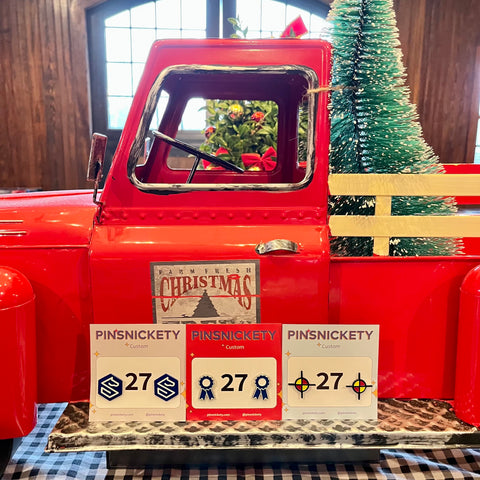 three pinsnickety custom horse show number pin designs in front of a christmas tree and a red holiday truck