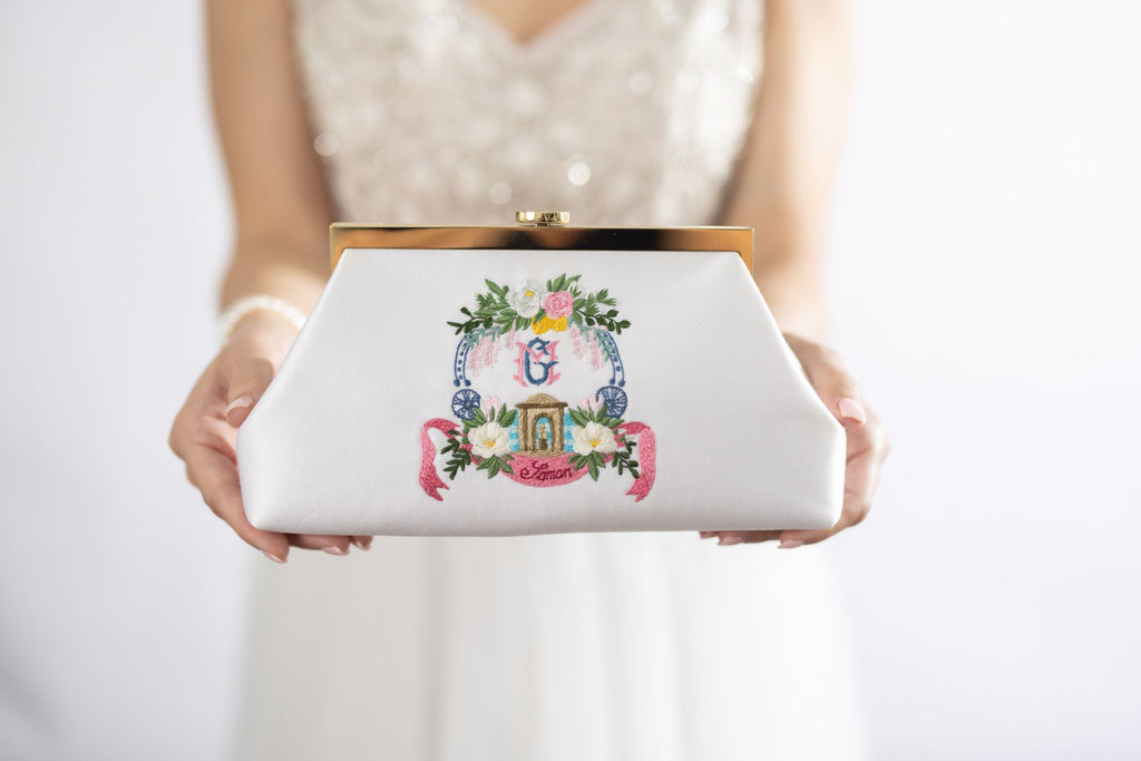 Woman in a white dress, holding a white rose a clutch in satin with custom embroidery, monogram for destinations wedding in Italy.