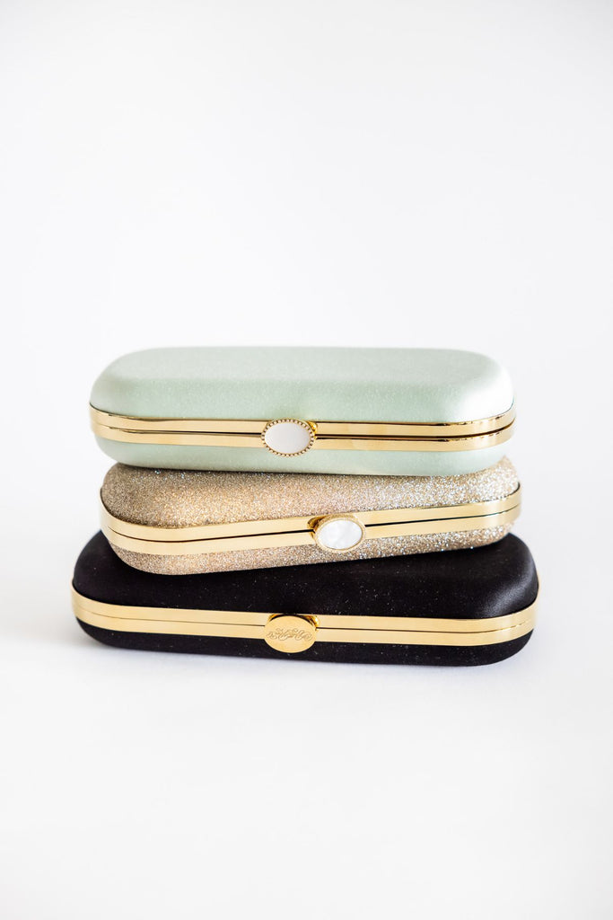 Three designer clutches stacked on top of each other, showing their side, top view with the clasp and hardware visible.