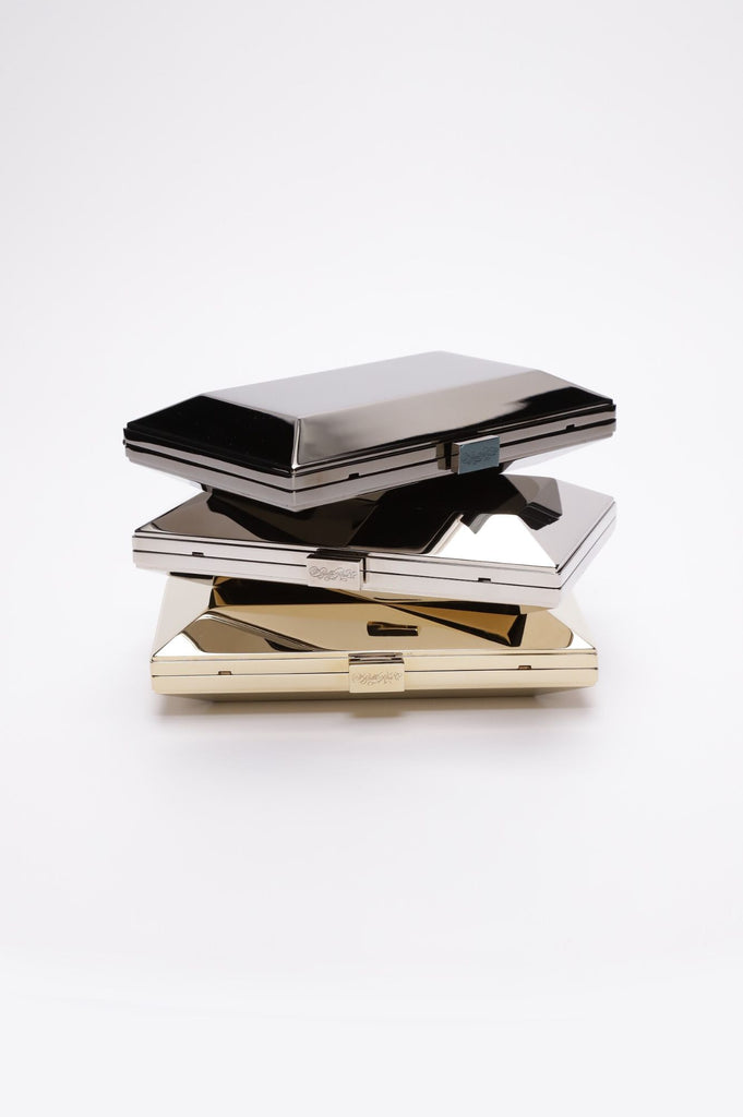 Three Milan Clutches in gunmetal, silver, and gold metallic stacked a top each other against white background.