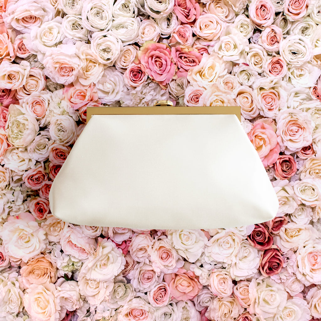 Rose Clutch in ivory laying flat on top a bed of red, pink and white roses.