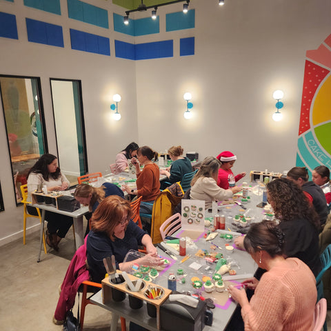 A group of people at multiple tables are decorating cupcakes during a do-it-yourself cupcake-decorating event at Cake Hoopla.