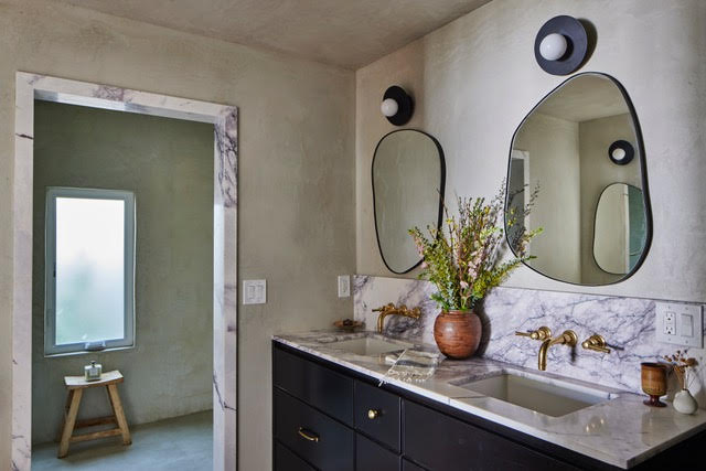 Modern bathroom with marble countertops, black cabinets, asymmetrical mirrors, and a potted plant.