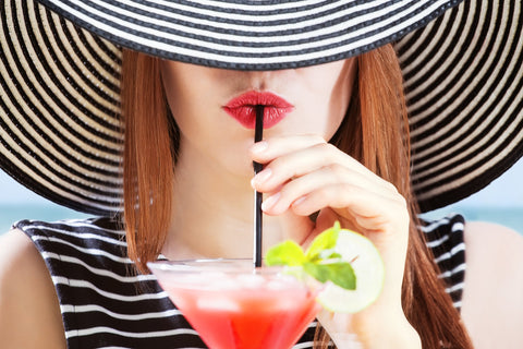 woman with straw sun hat and red lipstick drinking cocktail with a straw