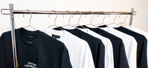 black and white t shirts hanging on a hanger with a white wall behind