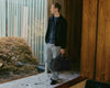 Man leans on wall inside retro looking apartment holding a brown briefcase