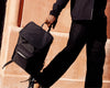 Man walks holding black nylon bag with brick building behind