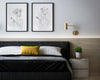 Hotel bed with minimalist paintings hung above, wooden panel and small plant on bedside table