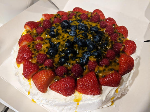 A pavlova topped with strawberries, raspberries, blueberries, and passionfruit pulp