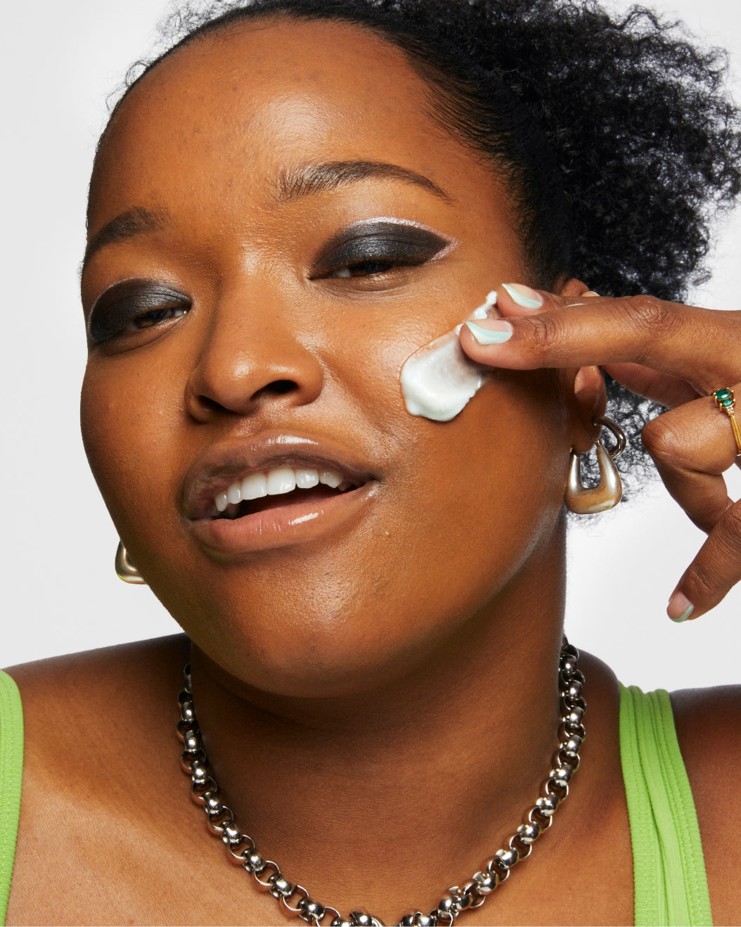 Model with makeup on applies a swipe of Milk Makeup Hydro Ungrip Cleansing Balm to their face against a white background.