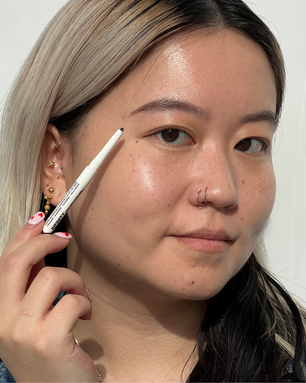 Model holds a Milk Makeup Infinity Long Wear Eyeliner against her face on a white background