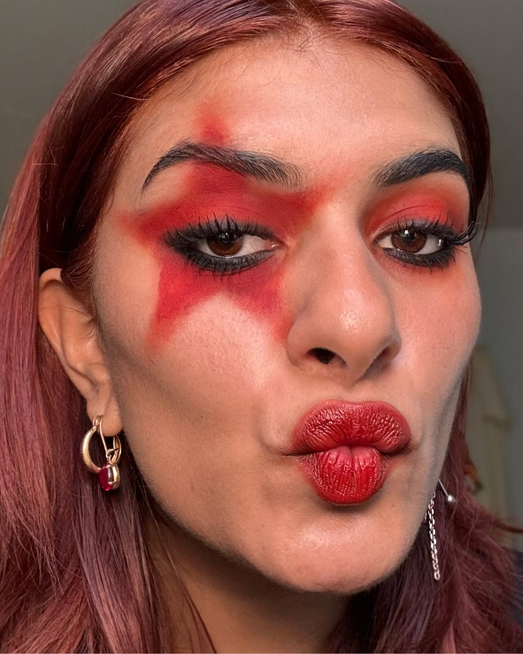 Model wears red star eye makeup and matching red lipstick