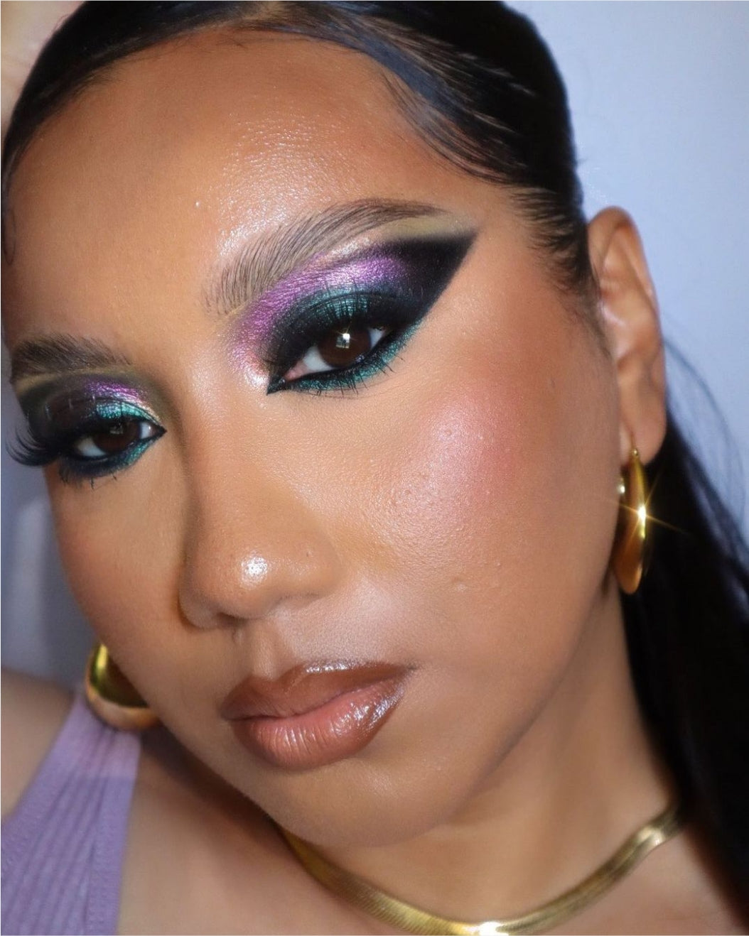 Portrait of a woman with jewel toned teal and purple makeup as part of a holiday makeup look.