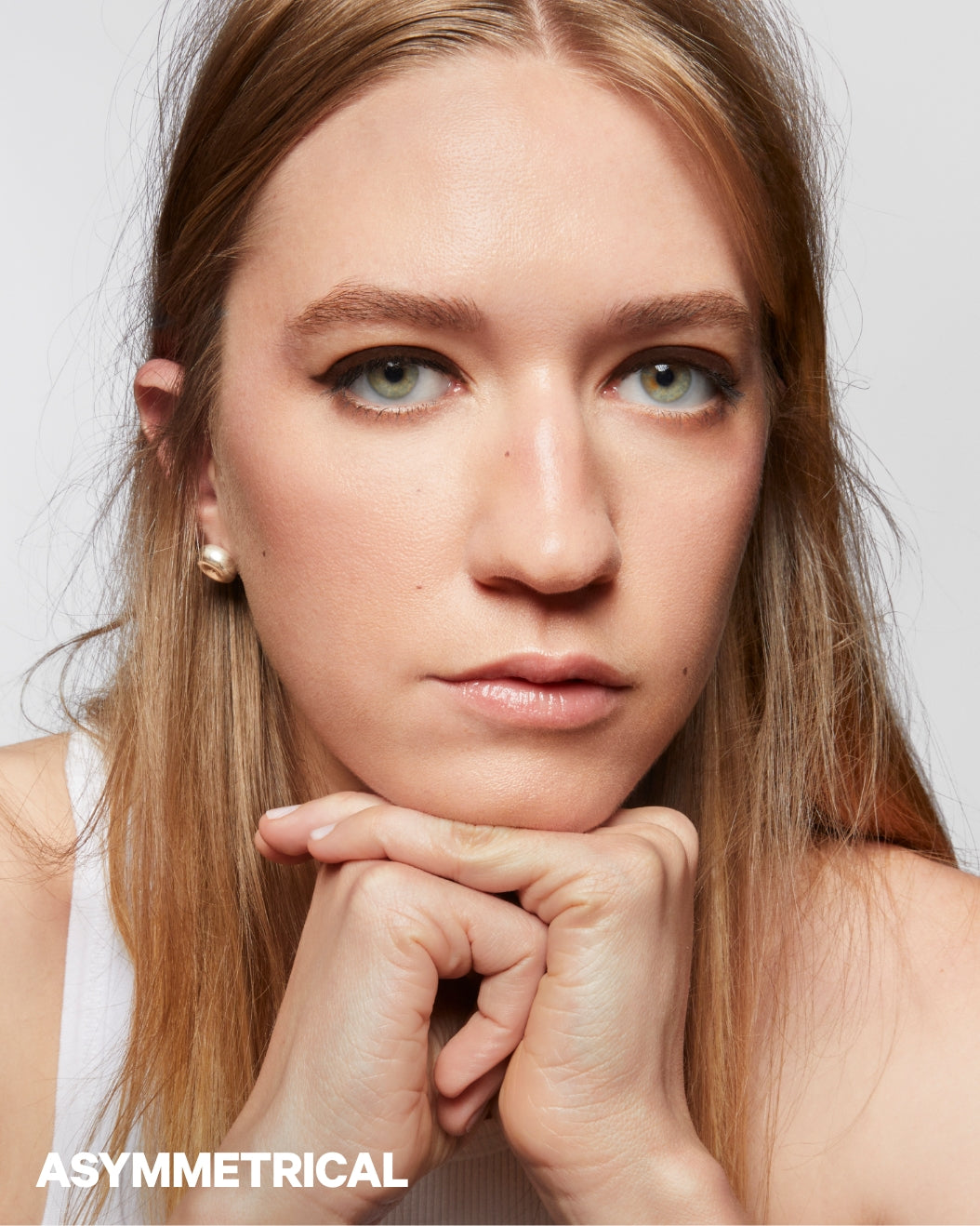 Model with asymmetrical eyes wears winged eyeliner on a white background
