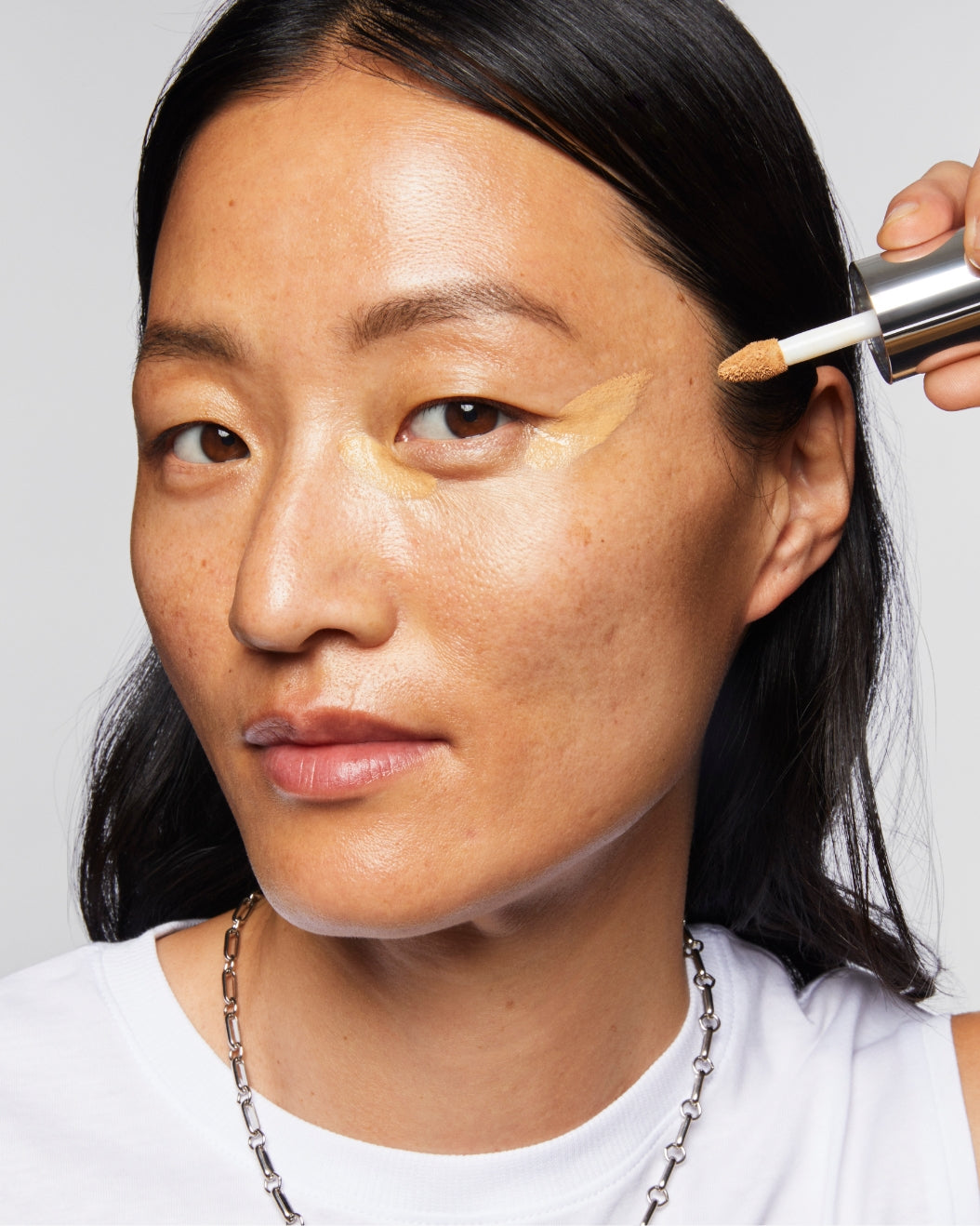 Model applies Milk Makeup Future Fluid Concealer on a white background