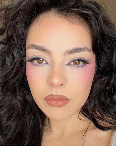 Selfie of a person wearing bright pink blush and blended cat-eye makeup with a nude lip