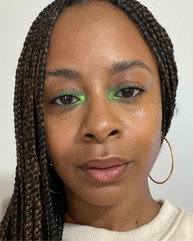 Portrait of a person with green inner corner eye shadow and nude glossy lips.
