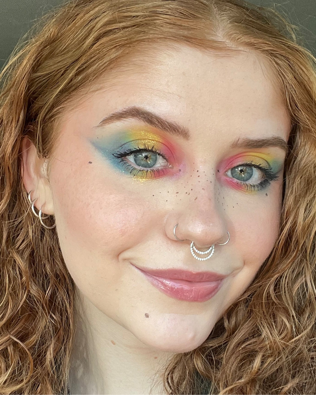 Selfie of a person with red hair wearing rainbow eyeshadow.