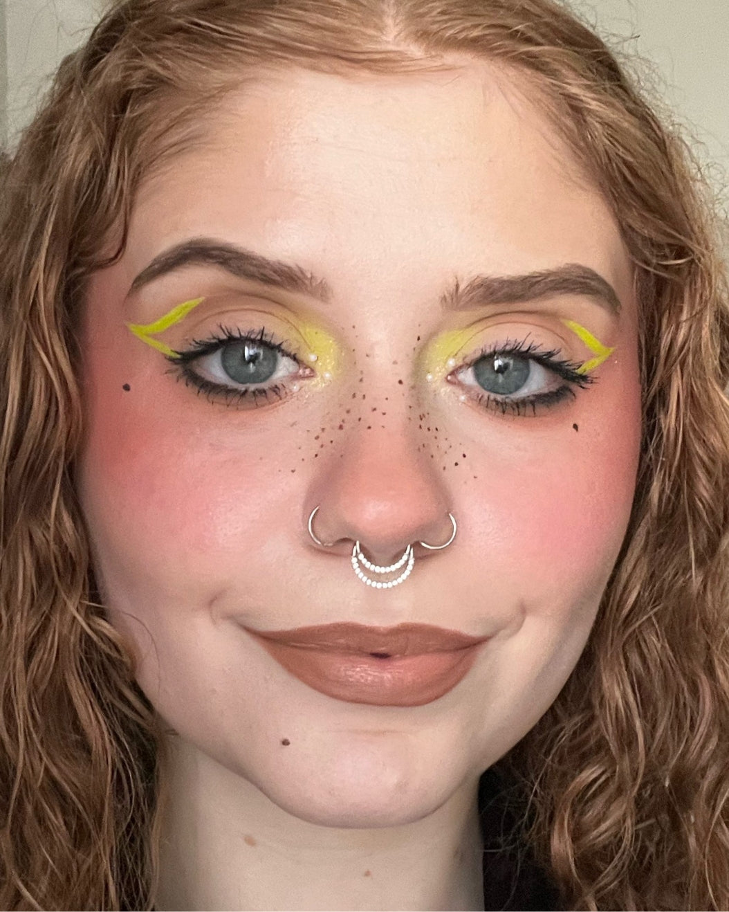 Selfie of a person with graphic neon yellow eye makeup.