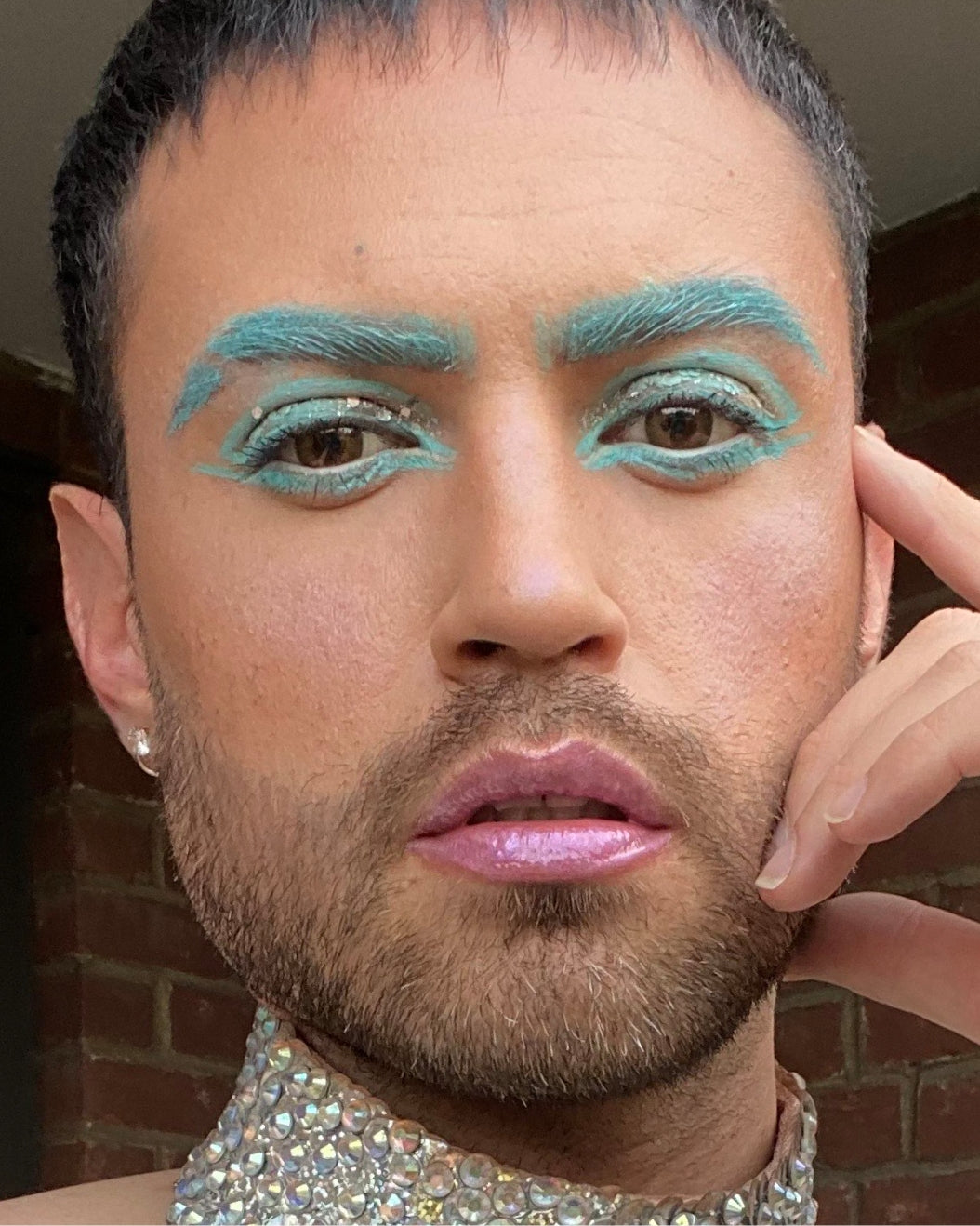 Selfie of a person in an iridescent fishscale top with seafoam eyebrows and matching liner.