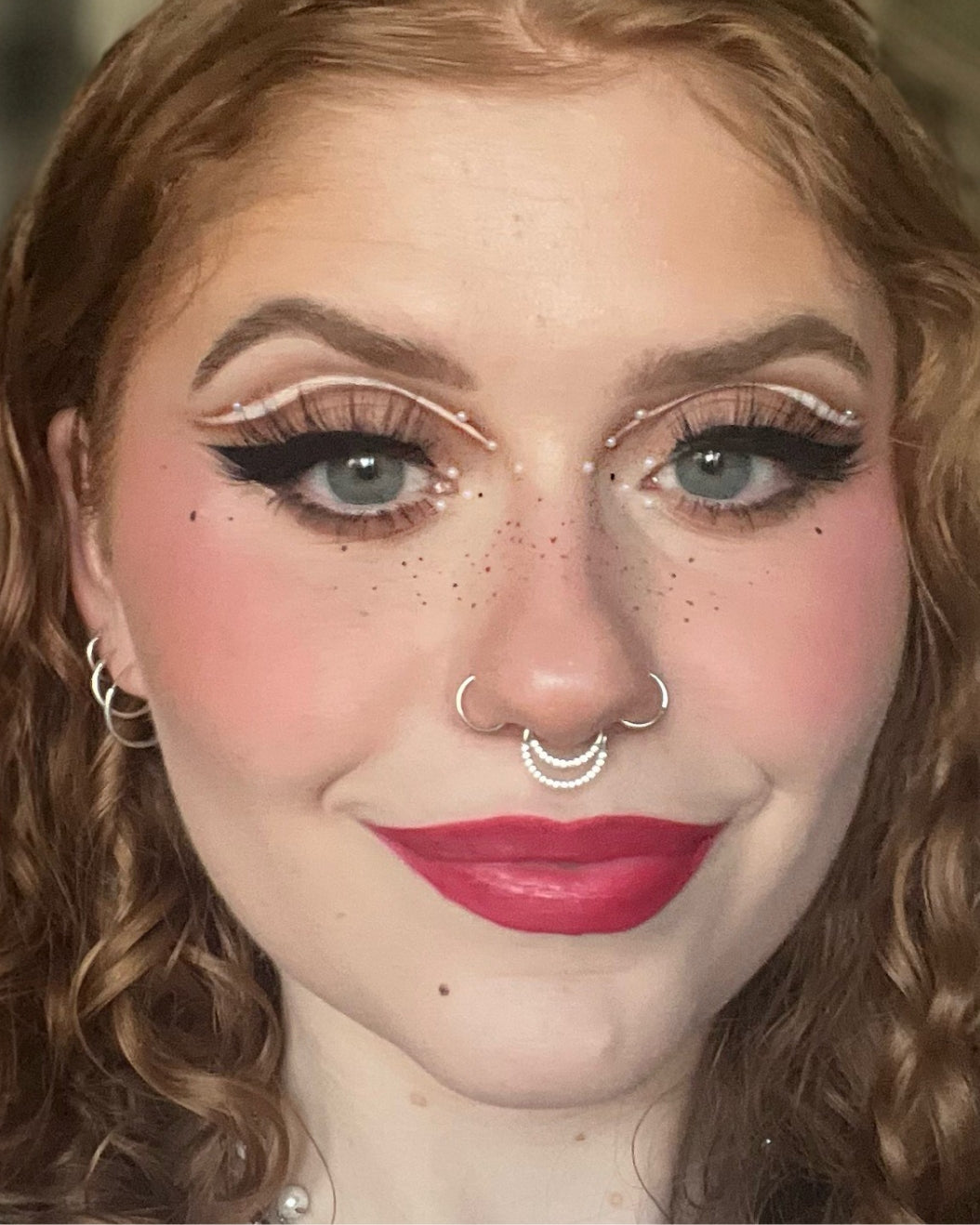 Photo of a person with red lipstick and graphic eye makeup with pearls.