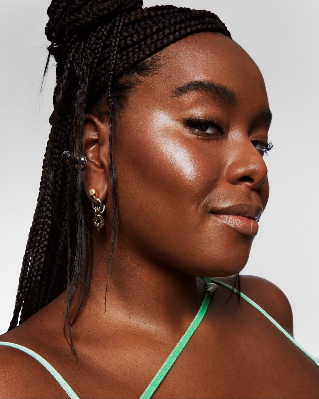 Model with a deep glowy complexion wears Milk Makeup Highlighter on a white background.