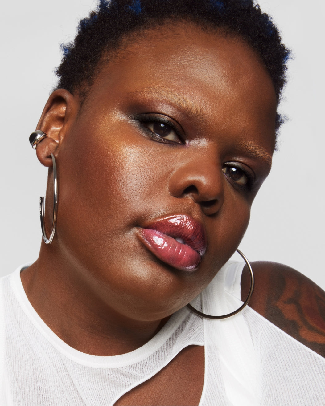 Model with a medium-deep skin tone wearing Milk Makeup Odyssey Lip Oil Gloss in Trek against a white background