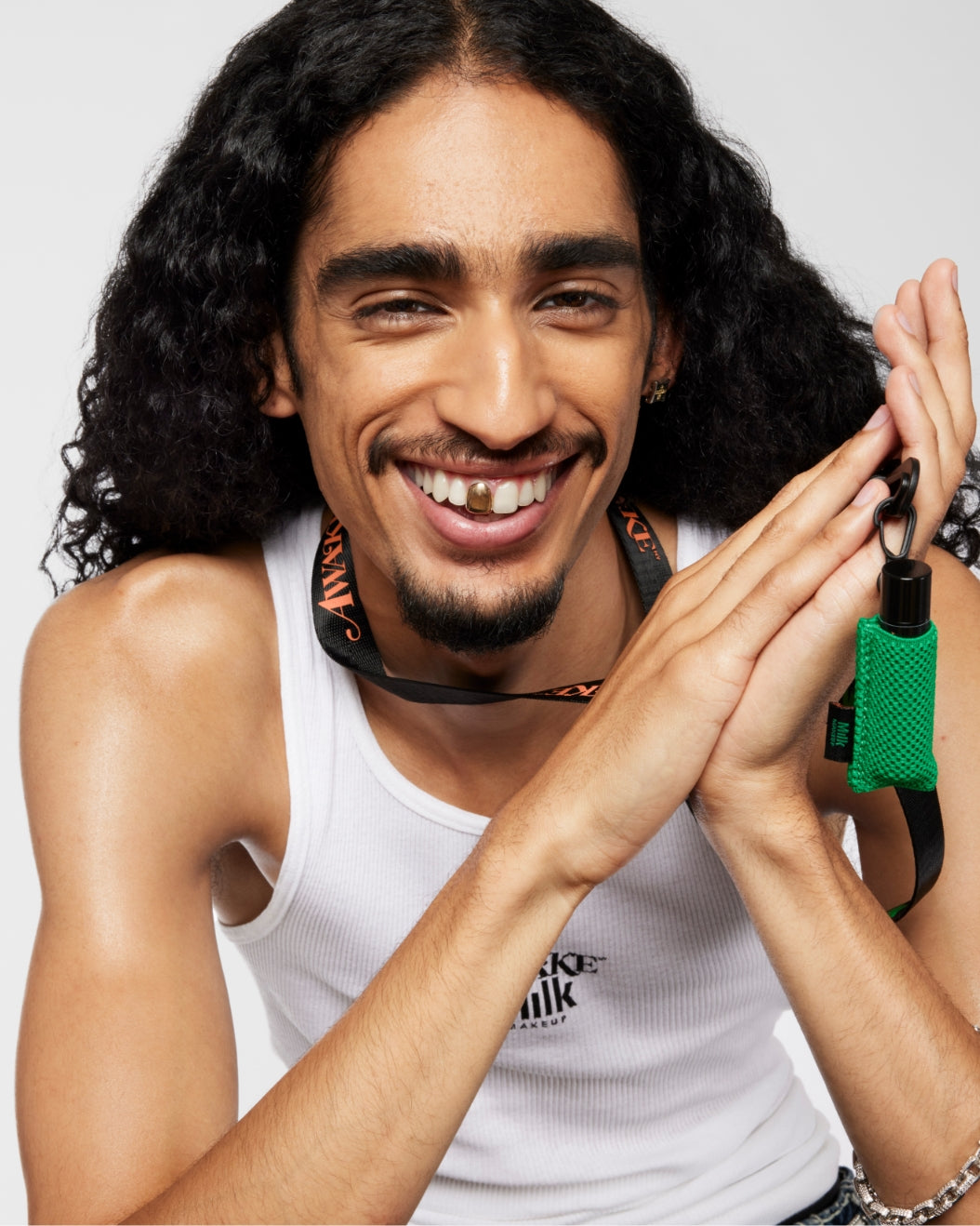 Model poses with Milk Makeup x Awake NY Lip Balm + Sleeve, plus lanyard on a white background.