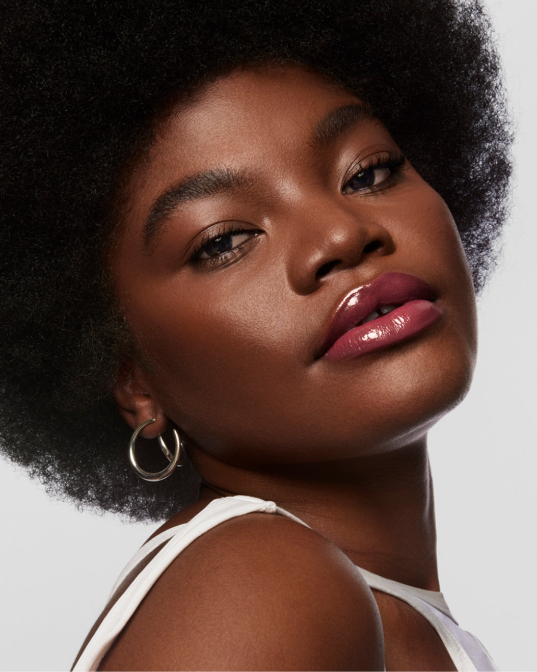Model wears Milk Makeup Odyssey Lip Oil Gloss in Trek on a white background