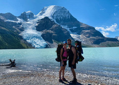 A young outdoor couple posing with their toddler in front of Mt. Robson in summer