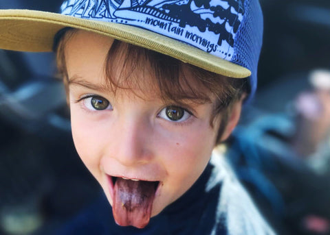 toddler with a tongue coloured from blueberries and with Ambler kid size hat looking at the camera