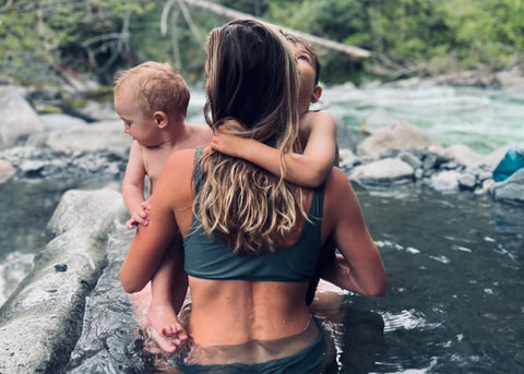 young mother sitting in a hot springs with her toddler and baby 