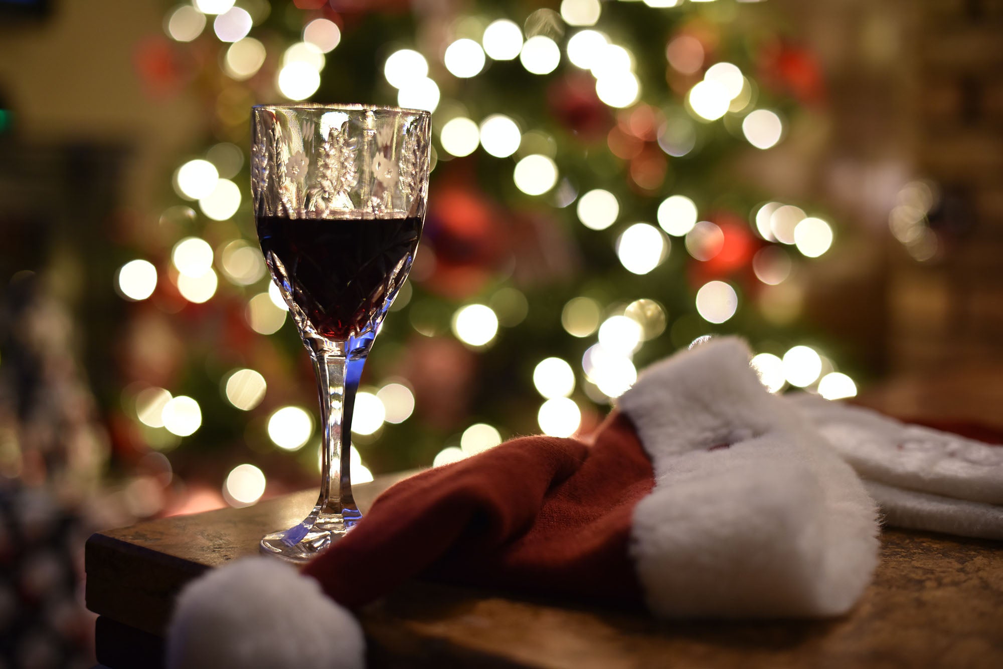 Glass of red wine next to Christmas tree and Santa hat