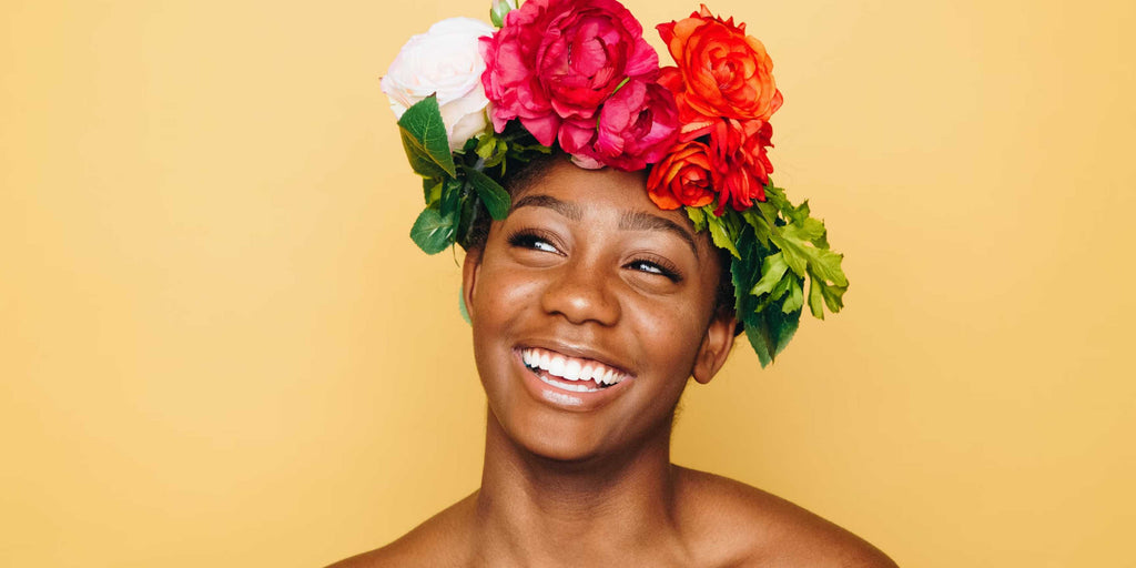Schwarze Frau mit Blumen am Kopf vor gelbem Hintergrund