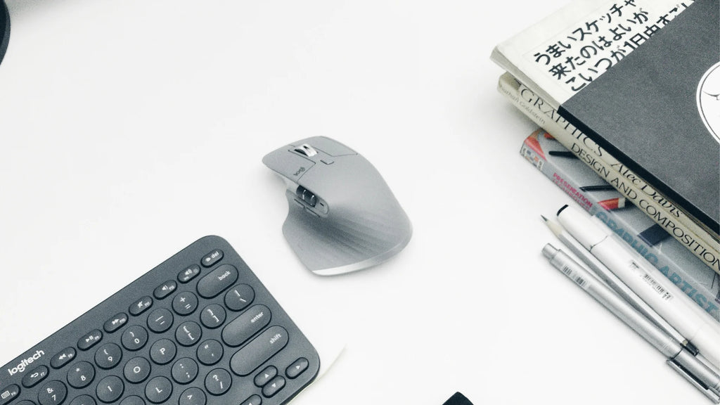 logitech mx master 3 mouse next to a keyboard and books