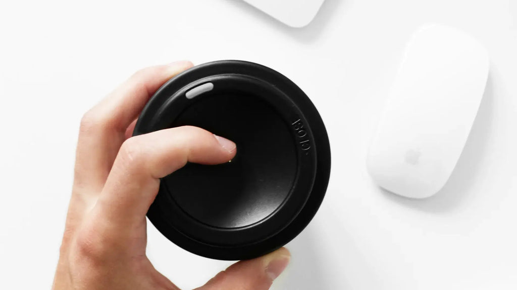 Hand on a coffee mug and a white Magic Mouse next to it