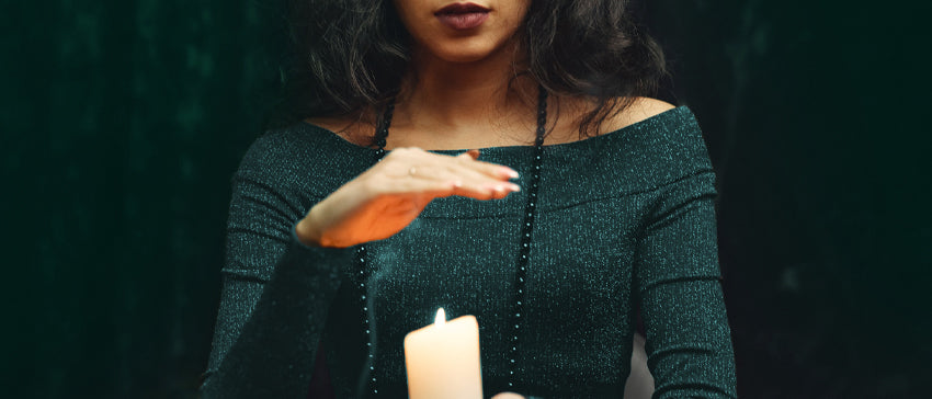 A person holding a candle with one hand, while hovering over the flame with their other hand