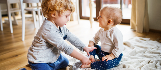 A baby and toddler interacting together.