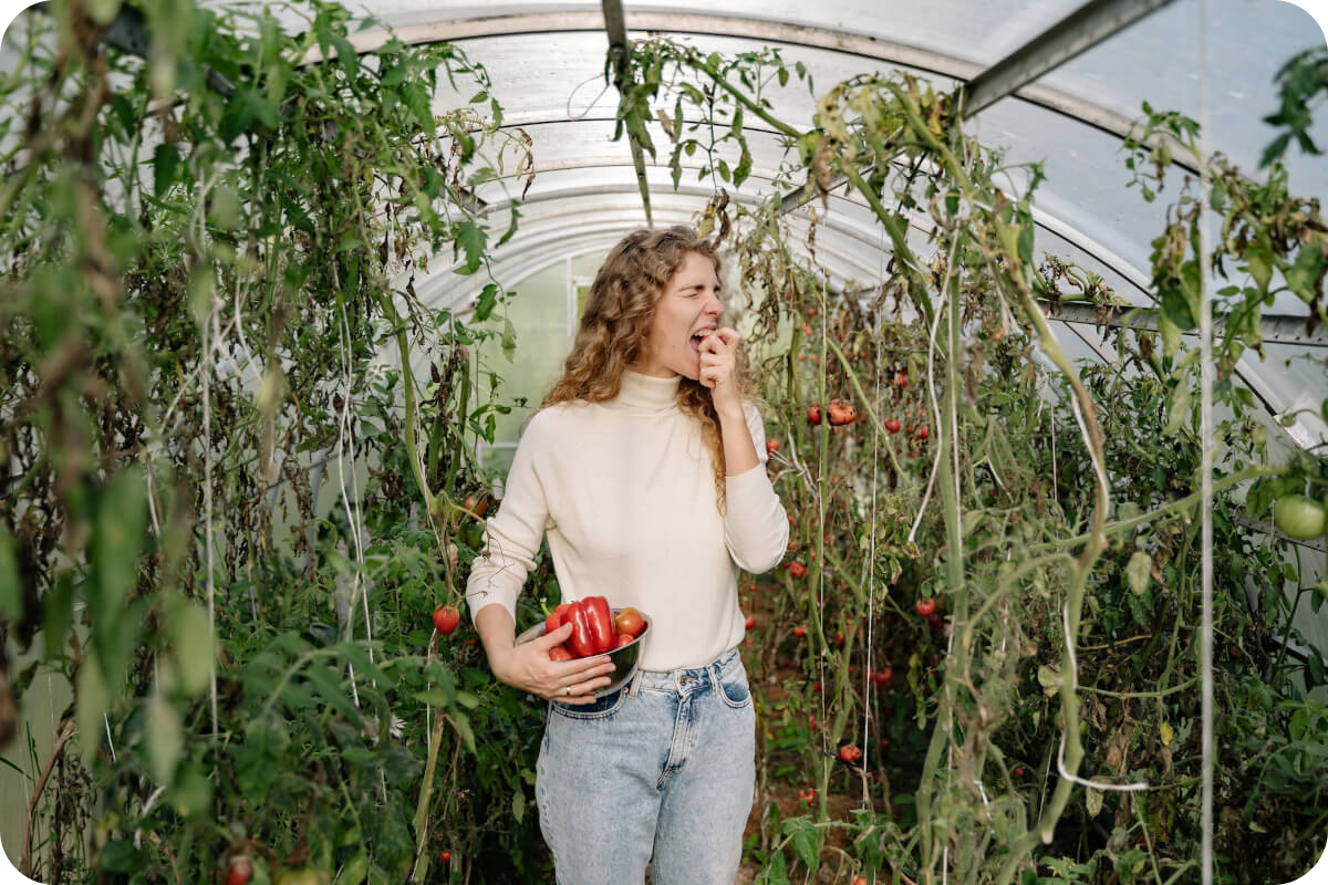 Frau vor einem Hintergrund üppiger Pflanzen, die in eine eisenreiche rote Paprika beißt, symbolisch für eine eisenbetonte, gesunde Ernährung und natürliche Eisenquellen.