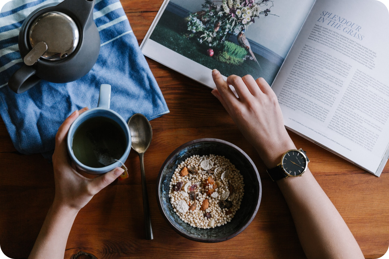 Tisch mit einem gesunden Frühstück bestehend aus Müsli und Tee neben einer aufgeschlagenen Zeitschrift, symbolisch für eine nahrhafte und energiereiche Morgenroutine, die zu einem produktiven Start in den Tag beiträgt.