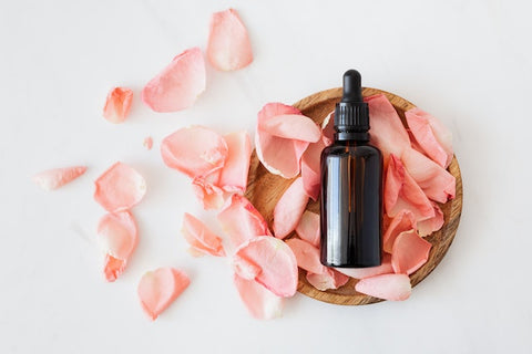 A cosmetic bottle on a wooden plate of pink rose petals 