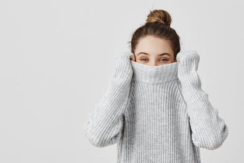 Woman in gray turtleneck sweater pulling it up over her mouth, with eyes peeking out