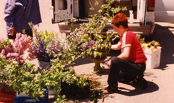 A person arranging flowers next to a van on a sunny day.
