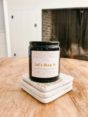 black chic candle from jj paperie & co, sitting in front of fire place for cozy fall aesthetic