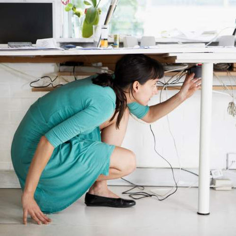 A woman under her work desk trying to organize cables