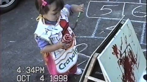 Mar as a toddler painting on an easel outside wearing a crayola smock.