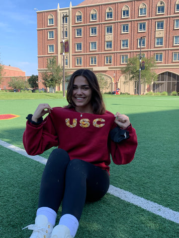 Mar's sister sitting at USC campus wearing a hand embroidered floral block letter sweatshirt