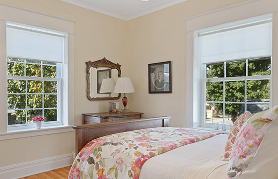 Cozy and sweet room decorates floral bedding, roller shades, wooden dresser.