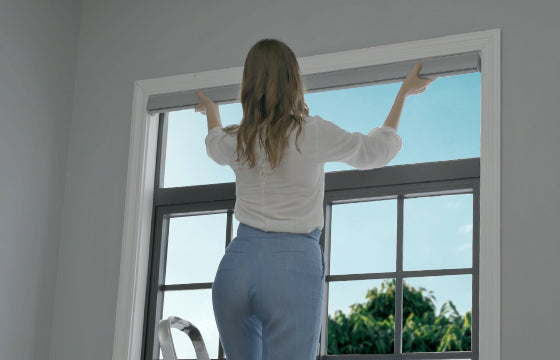 A woman is mounting the shade to the top of the window frame